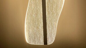 A modern, abstract light fixture with a textured surface and a central dark stripe.