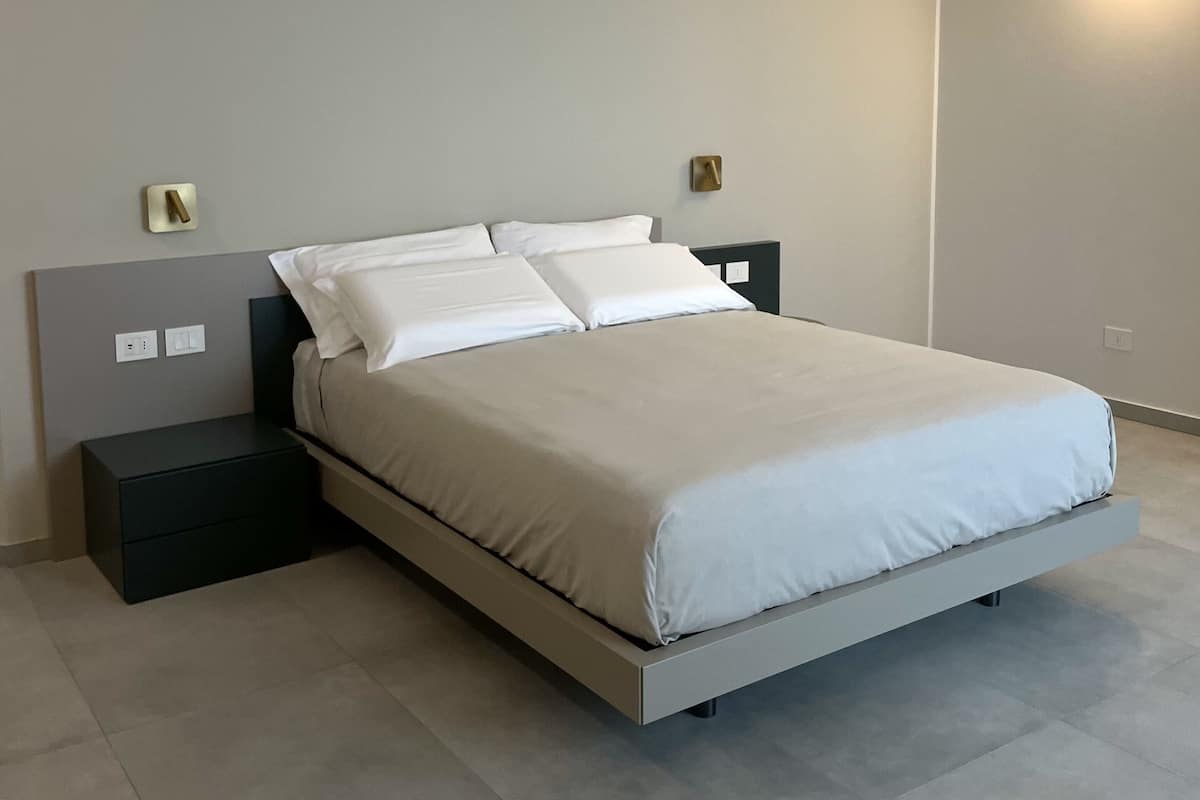 A modern bedroom with a bed, nightstands, and a wall-mounted light fixture.