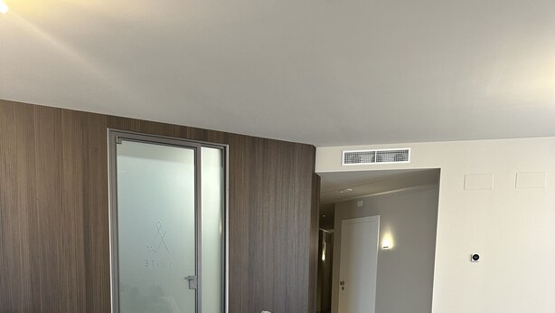 A modern living room with a large sectional sofa, a glass door leading to a balcony, and a wooden panel wall.