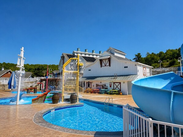 A swimming pool with a water play area, a large blue boat, and a white building with a barn-like structure. - Huge 4-bedroom cottage at Stormy Point. Near attractions. Family Friendly. (Branson)