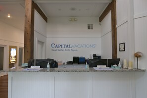 Ein Empfangsschalter mit einem Schild, auf dem 'CAPITALVACATIONS' und der Slogan 'Reisen. Treffen. Lächeln. Wiederholen.' steht.