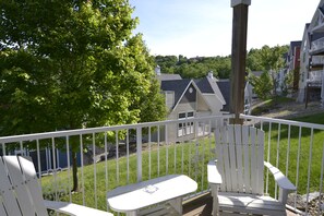Ein Balkon mit weißen Geländern, einem weißen Adirondack-Stuhl und Blick auf eine Wohngegend mit Häusern und Bäumen.