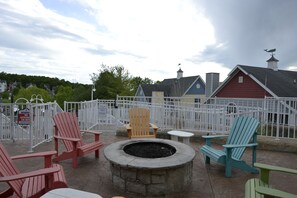 A patio area with Adirondack chairs, a fire pit, and a view of a red building with a weather vane.