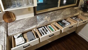 A kitchen with a granite countertop, wooden cutting board, and multiple drawers containing kitchen utensils. - Cox Riverside Retreat - 32 miles to Springfield (Buffalo)