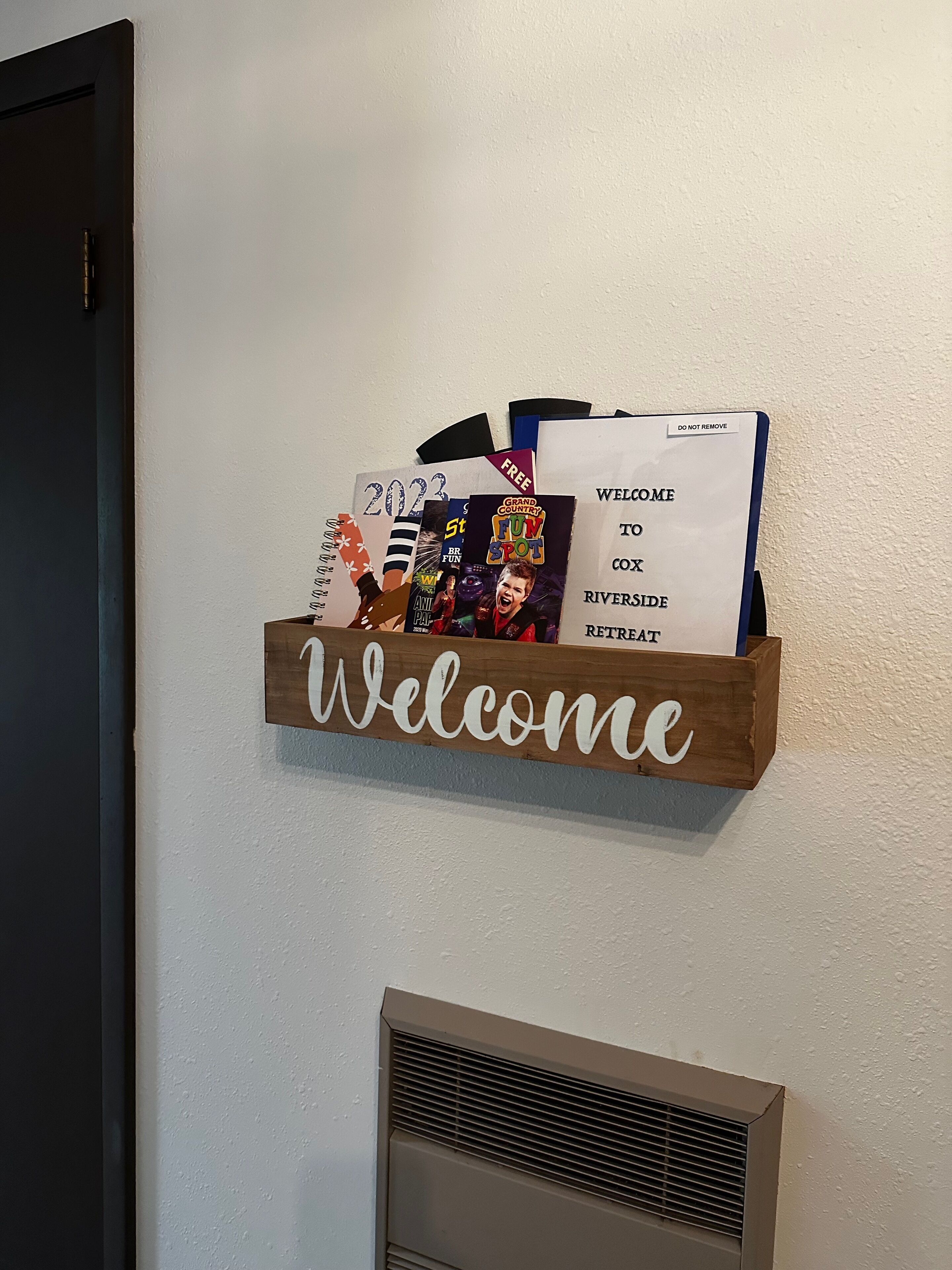 A welcome sign with a wooden frame and a wall-mounted vent below it.