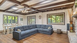 A modern living room with a sectional sofa, wooden flooring, large windows, and a dining area. - Cox Riverside Retreat - 32 miles to Springfield (Buffalo)