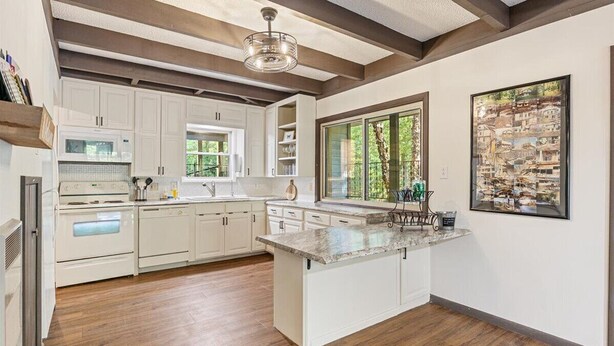 A modern kitchen with white cabinetry, a large island, and a view of greenery through a window. - Cox Riverside Retreat - 32 miles to Springfield (Buffalo)