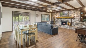 A spacious living room with a fireplace, wooden beams on the ceiling, and a dining area with chairs and a table. - Cox Riverside Retreat - 32 miles to Springfield (Buffalo)