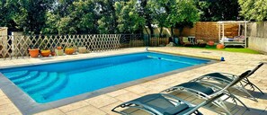 A swimming pool with a wooden deck, lounge chairs, and a wooden fence.