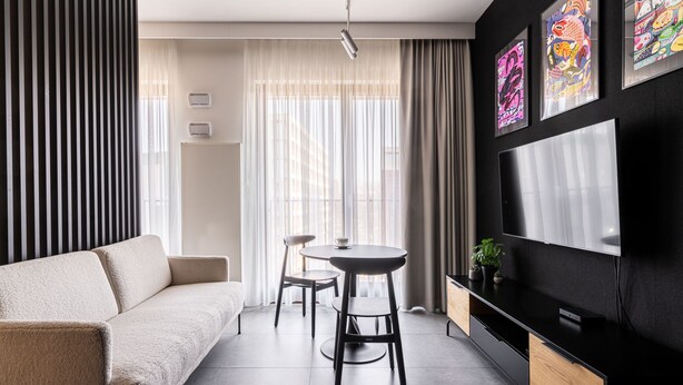 A modern living room with a sofa, a dining table with two chairs, a TV, and artwork on the wall. - RentPlanet - Apartament Śrutowa (Wroclaw)