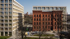 A modern building with a flat roof and large windows, adjacent to a historic red brick building with a central entrance and multiple windows. - RentPlanet - Apartament Śrutowa (Wroclaw)