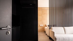 A modern room with a black door, a sofa, and a wooden slat partition. - RentPlanet - Apartament Śrutowa (Wroclaw)