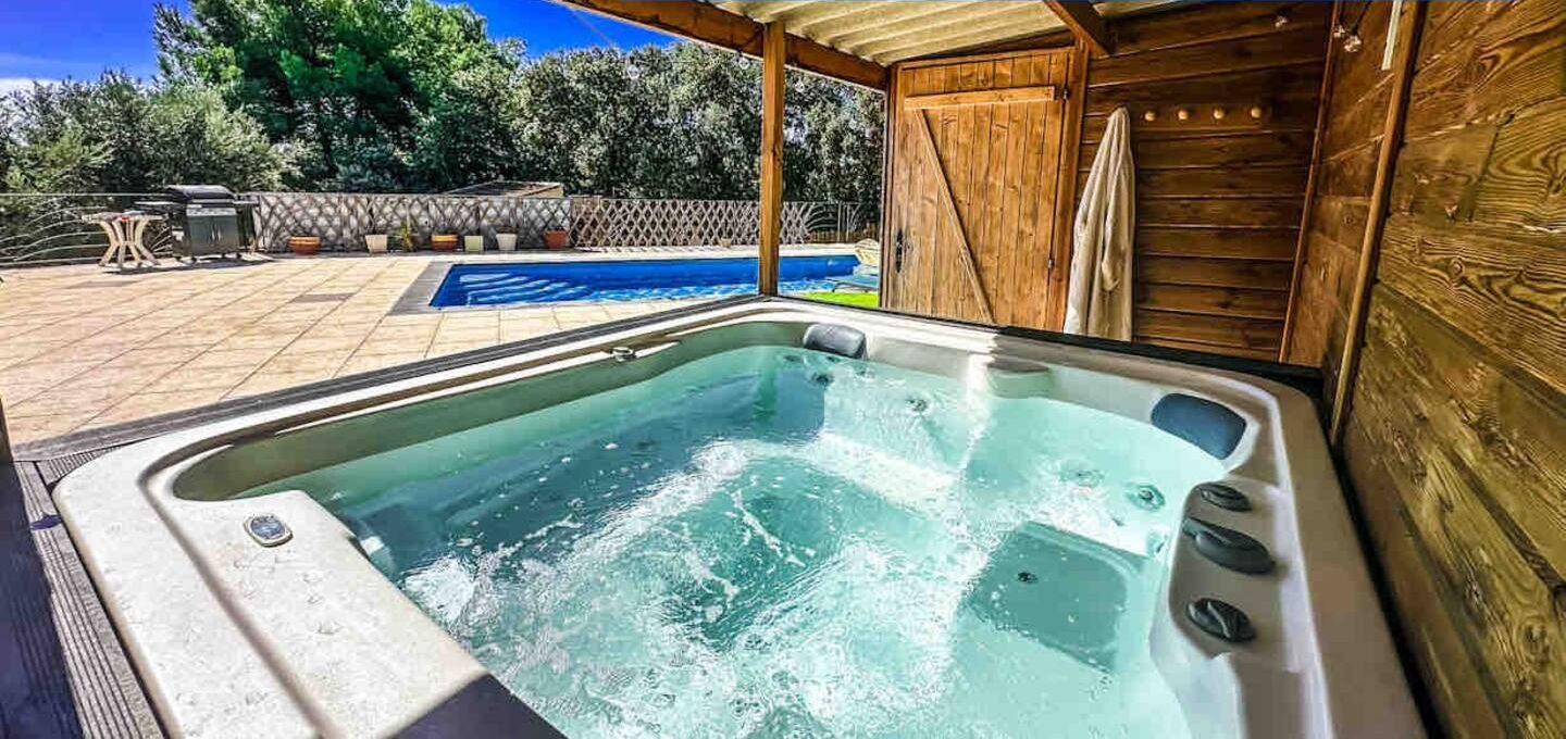 A hot tub with a wooden deck and a pool in the background.