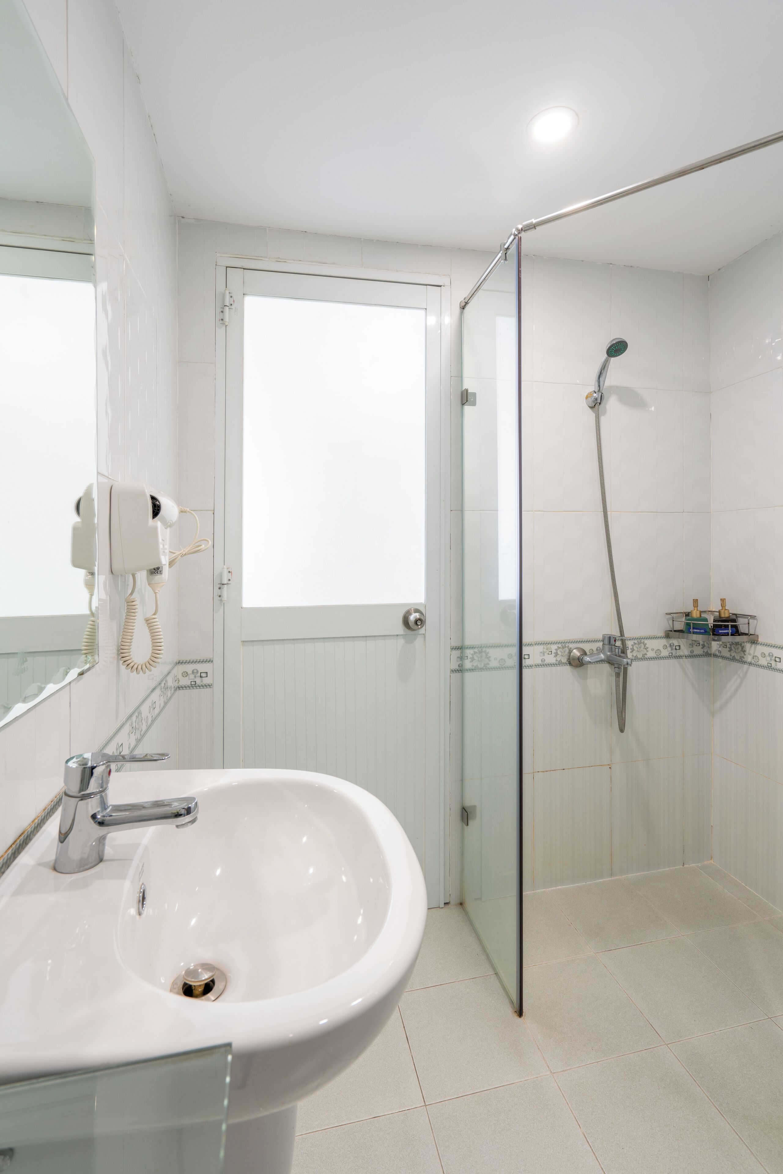 A bathroom with a glass shower enclosure, a white sink, and a hairdryer mounted on the wall.