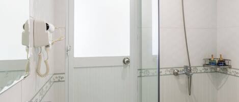A bathroom with a glass shower enclosure, a white sink, and a hairdryer mounted on the wall.