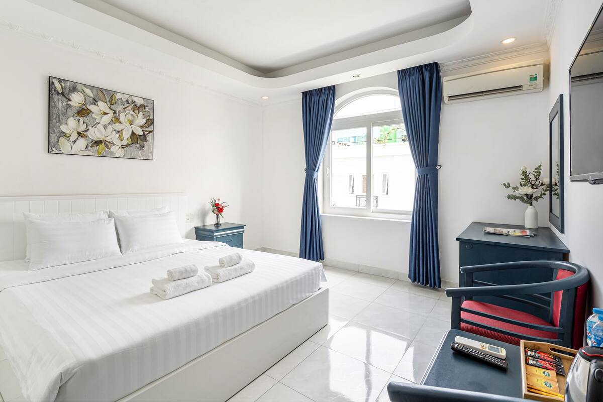 Une chambre d’hôtel avec un grand lit, un bureau avec une chaise, un tableau au mur et une fenêtre avec des rideaux.