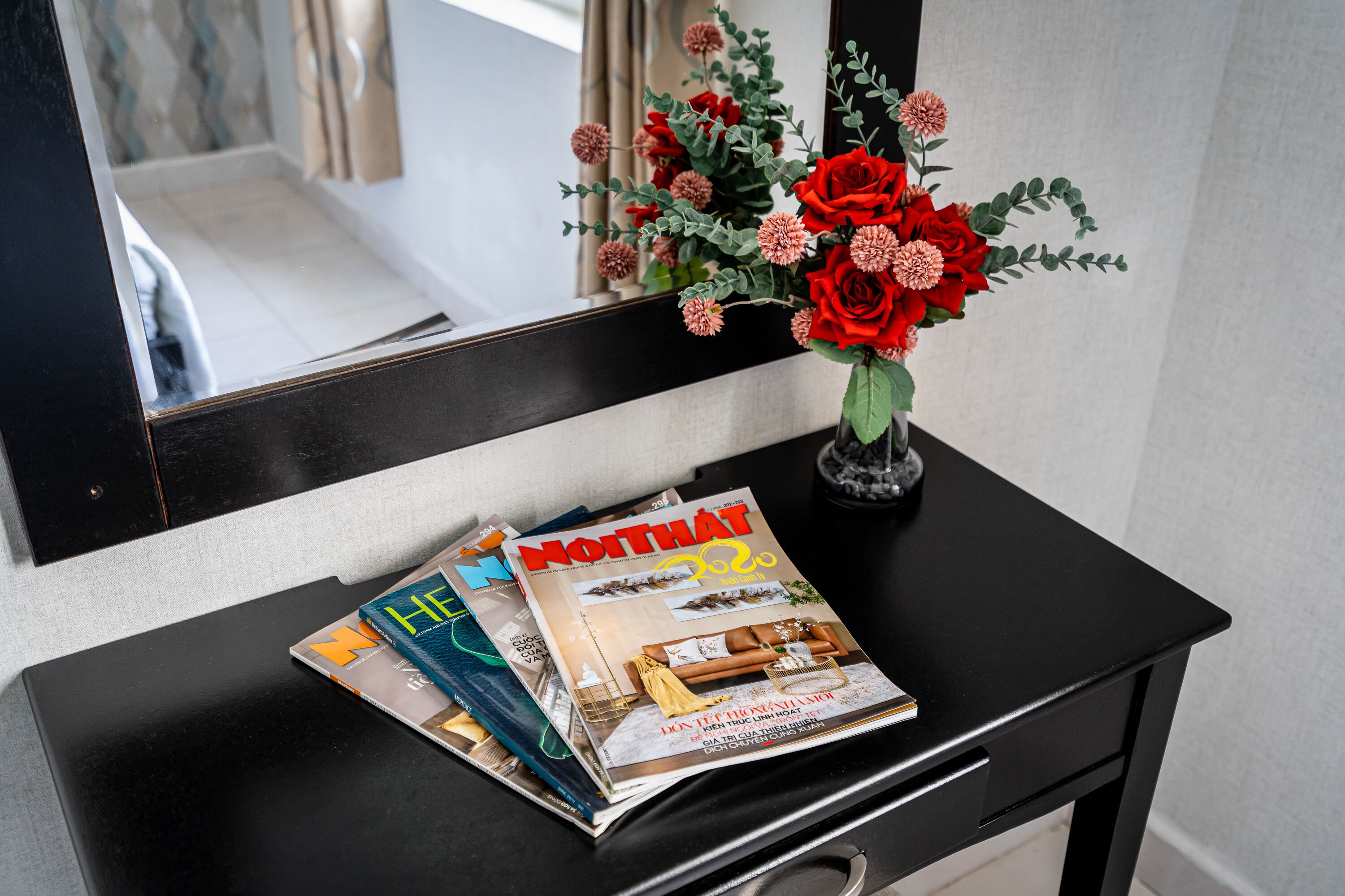 A black desk with a magazine and a vase of flowers.
