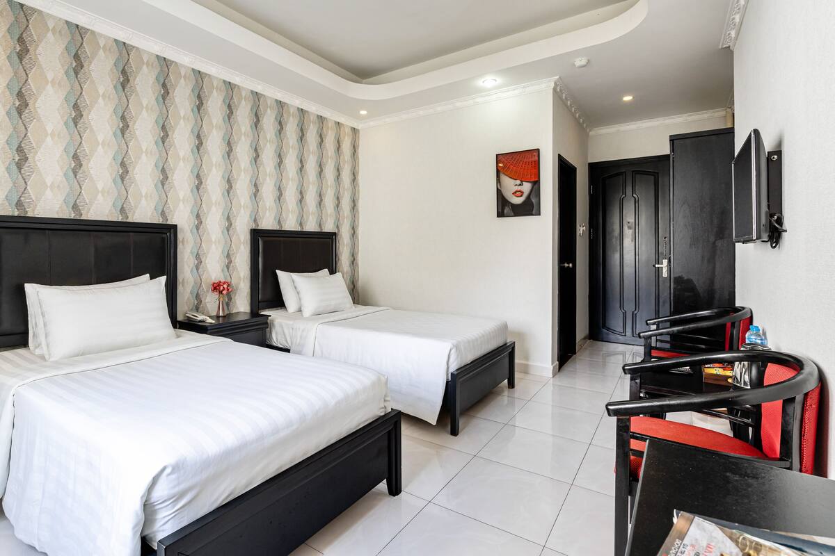 Une chambre d’hôtel avec deux lits, une petite table sur laquelle se trouve un vase, un tableau accroché au mur et un téléviseur fixé au mur.