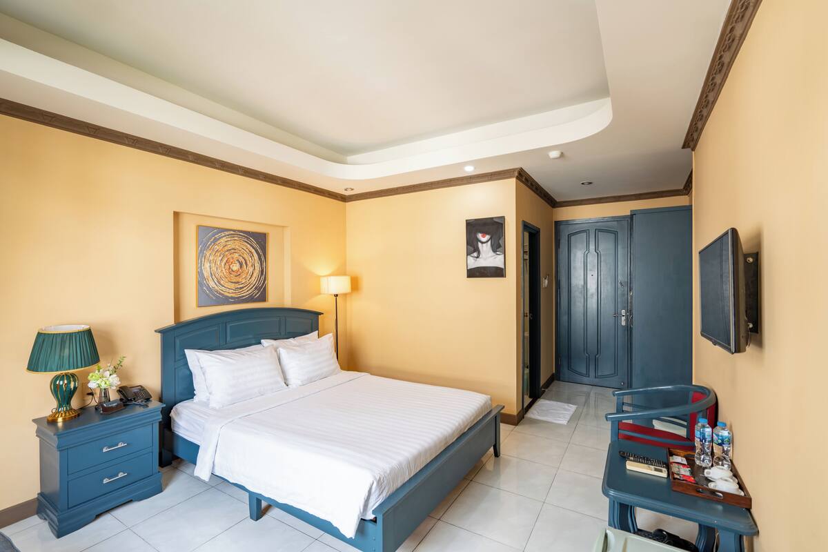 Une chambre à coucher comprenant un lit, une table de chevet, une lampe, des œuvres d’art, une armoire et un bureau avec des objets.