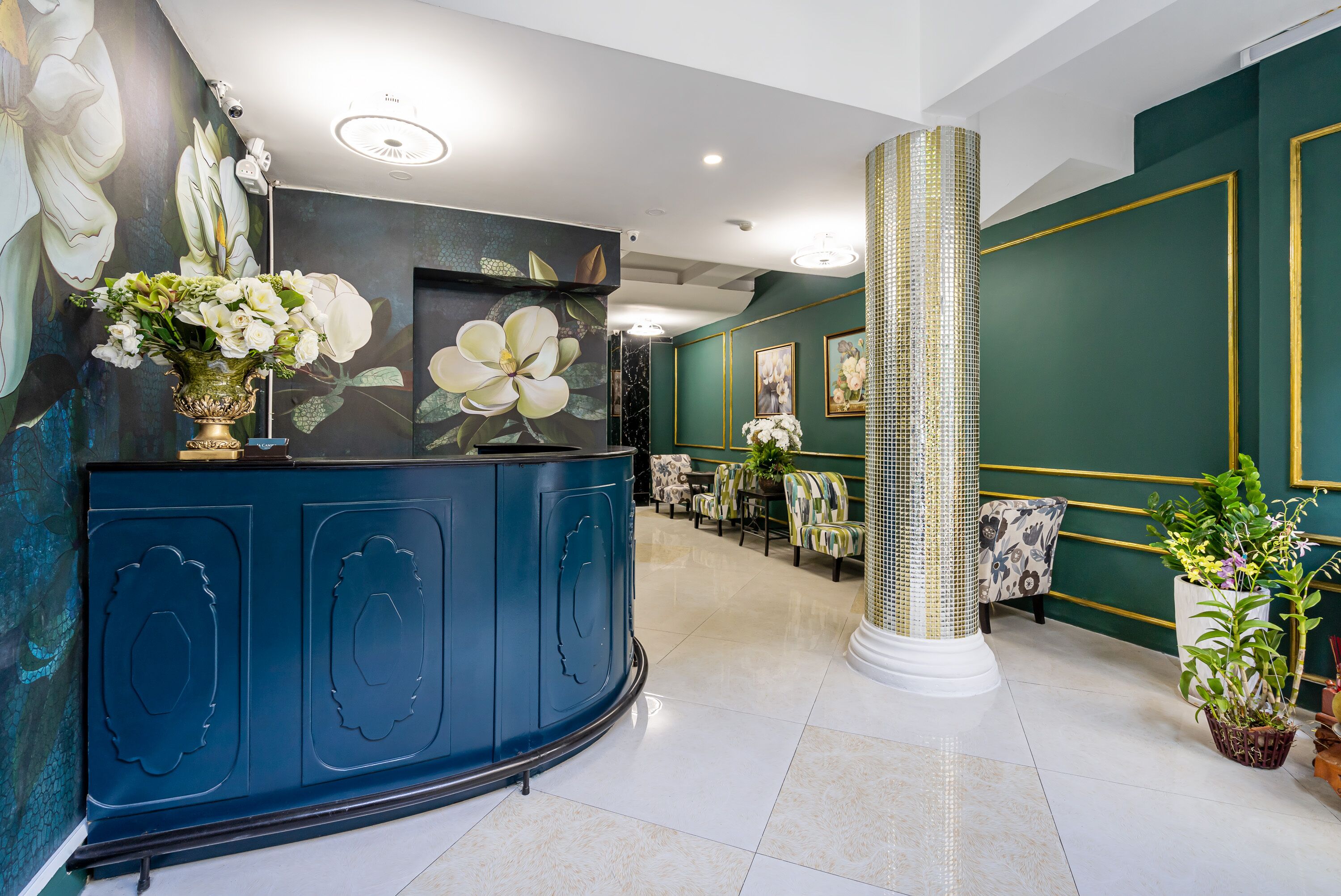 Un área de recepción con un mostrador azul, un cuadro floral grande y un alto pilar decorativo.