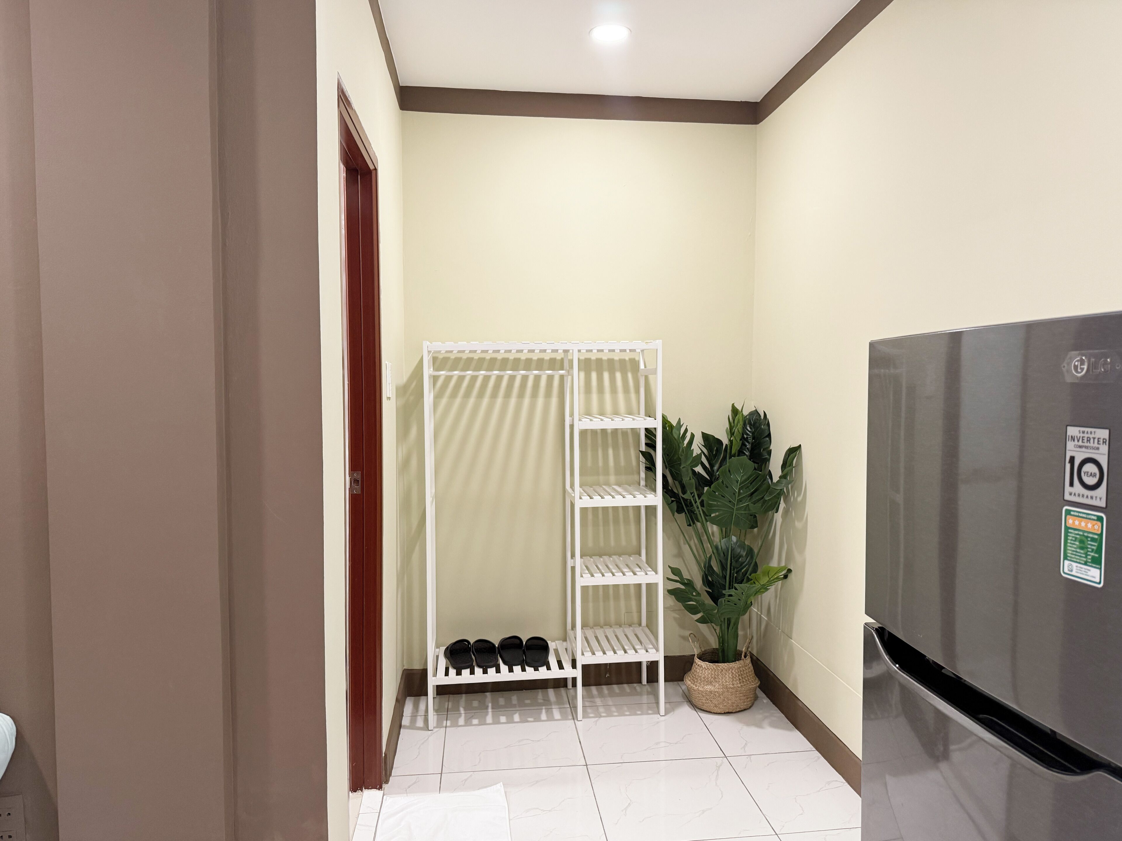 A compact kitchen with a refrigerator, a white shoe rack, and a potted plant.