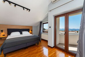 A bedroom with a bed, bedside lamps, a window with a view, and a sliding glass door to a balcony. - Villa Bruna (Zadar)