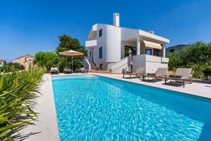 Uma casa moderna com piscina, espreguiçadeiras e uma escadaria que leva ao andar superior.