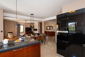 A modern kitchen with a large island, dining area with chairs and a table, and a living room with a fireplace. - Villa Bruna (Zadar)