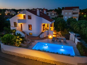 Une maison moderne à deux étages, dotée d’une piscine, d’un espace extérieur aménagé et d’une entrée bien éclairée.