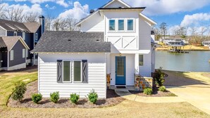A two-story house with a front porch, a garage, and a small front yard with a lawn and shrubs. - Changes in Latitude by Lake Martin Vibe (Dadeville)