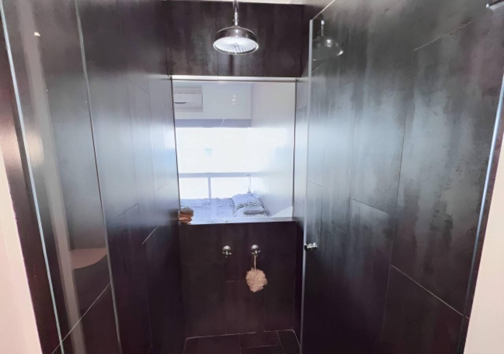 A modern bathroom with a walk-in shower, dark tiles, and a visible window.