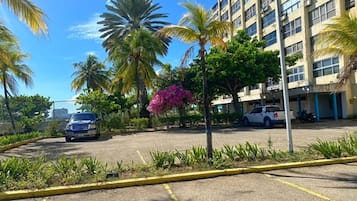 A parking lot with a blue car, surrounded by palm trees and a building with multiple windows.