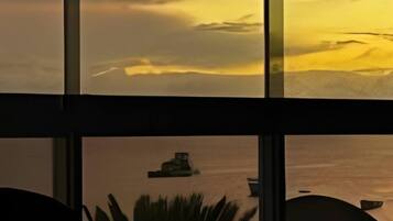 A view through a window with a boat on the water, a plant in the foreground, and a building in the background.