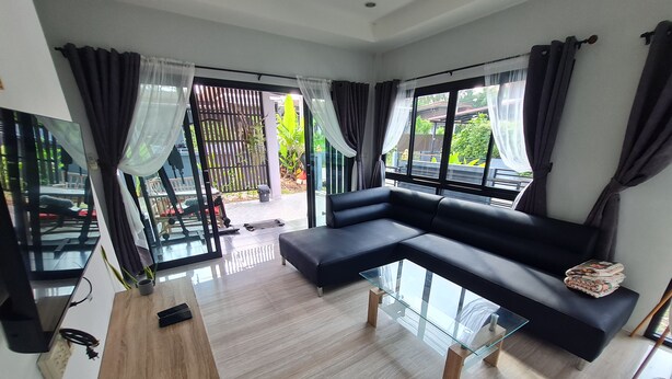 A modern living room with a sectional sofa, a glass coffee table, and a TV on a stand. - D&A Paradise Villas (Koh Samui)