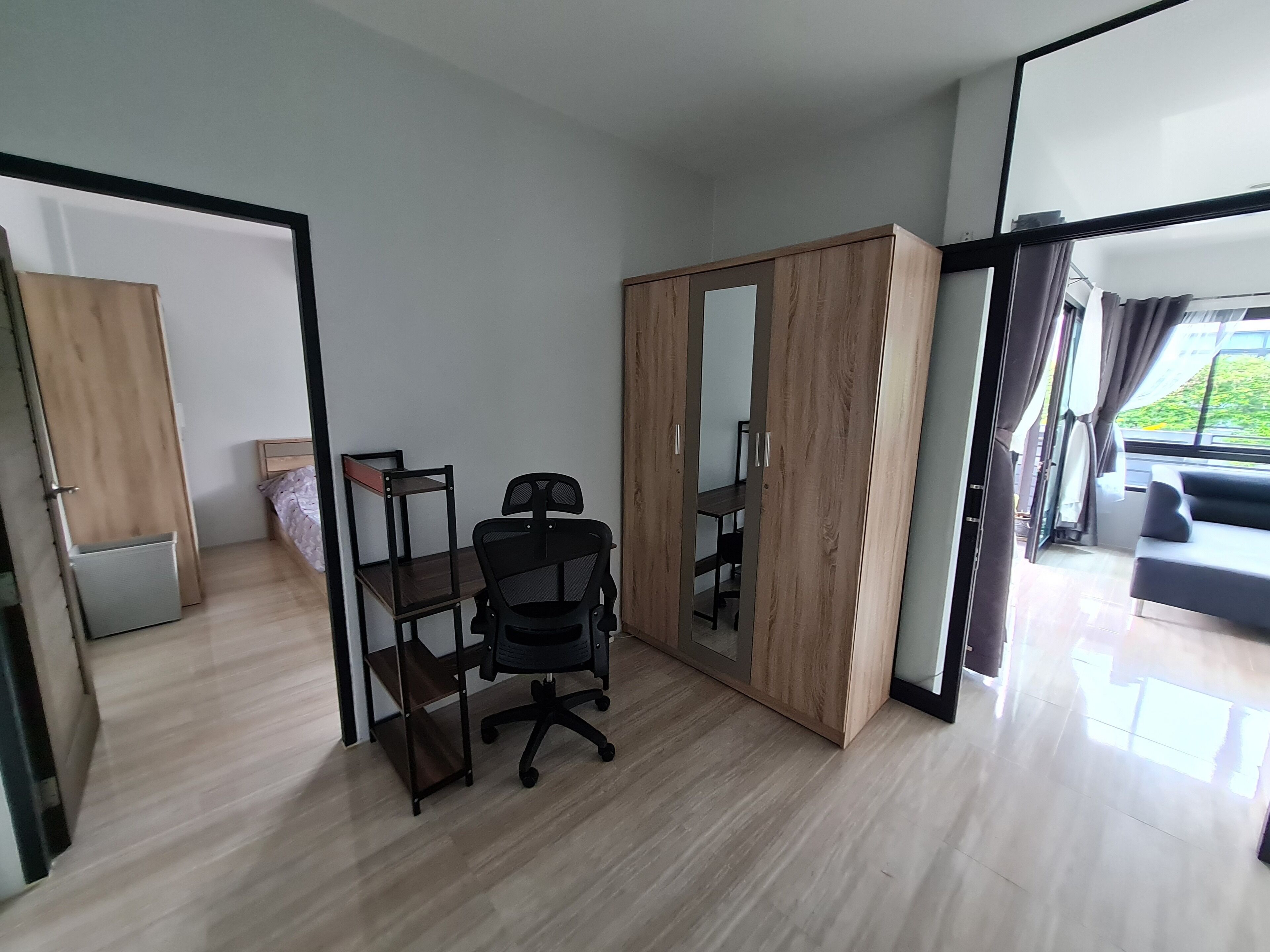 Een moderne kamer met een houten vloer, een zwarte bureaustoel, een houten garderobe en een grote spiegel.