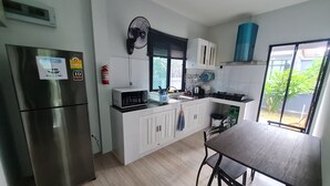A modern kitchen with white cabinets, a stainless steel refrigerator, a microwave, and a gas stove. There is a window providing natural light and a view of greenery outside. - D&A Paradise Villas (Koh Samui)
