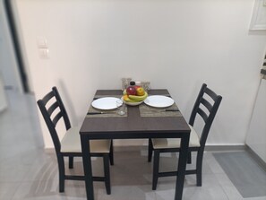 Een eettafel met twee stoelen, een schaal fruit en twee borden.