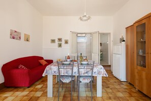 A dining area with a table set for four, a red sofa, and a wooden cabinet. - 3766 Appartamento Ilde by Barbarhouse (Porto Cesareo)