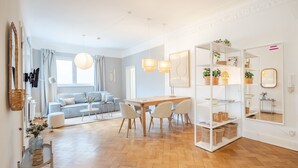 Un salon moderne avec un canapé, une table à manger et des chaises. On y trouve des étagères ornées de plantes et de paniers.