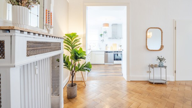 Une cuisine moderne avec des meubles blancs, un parquet en bois disposé en chevrons et une vue sur la salle à manger.