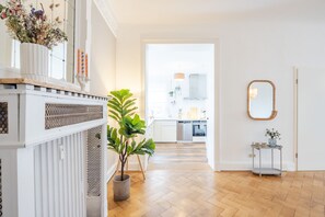 A modern kitchen with white cabinets, a wooden herringbone floor, and a view into the dining area. - Schanzenwohnung "tender" (Hamburg)