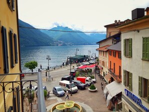A street view with a lake, buildings, and parked cars. - Al Pontile (Argegno)