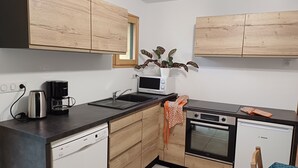 A compact kitchen with a Bosch dishwasher, a microwave, and an oven. There is a wooden cabinet above the sink and a potted plant on the counter. - In the Sweet Orchard of the Doubs ***** (Fertans)