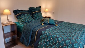 A neatly made bed with a teal and dark blue floral pattern, flanked by two bedside tables with lamps, one of which has a book on it. - In the Sweet Orchard of the Doubs ***** (Fertans)
