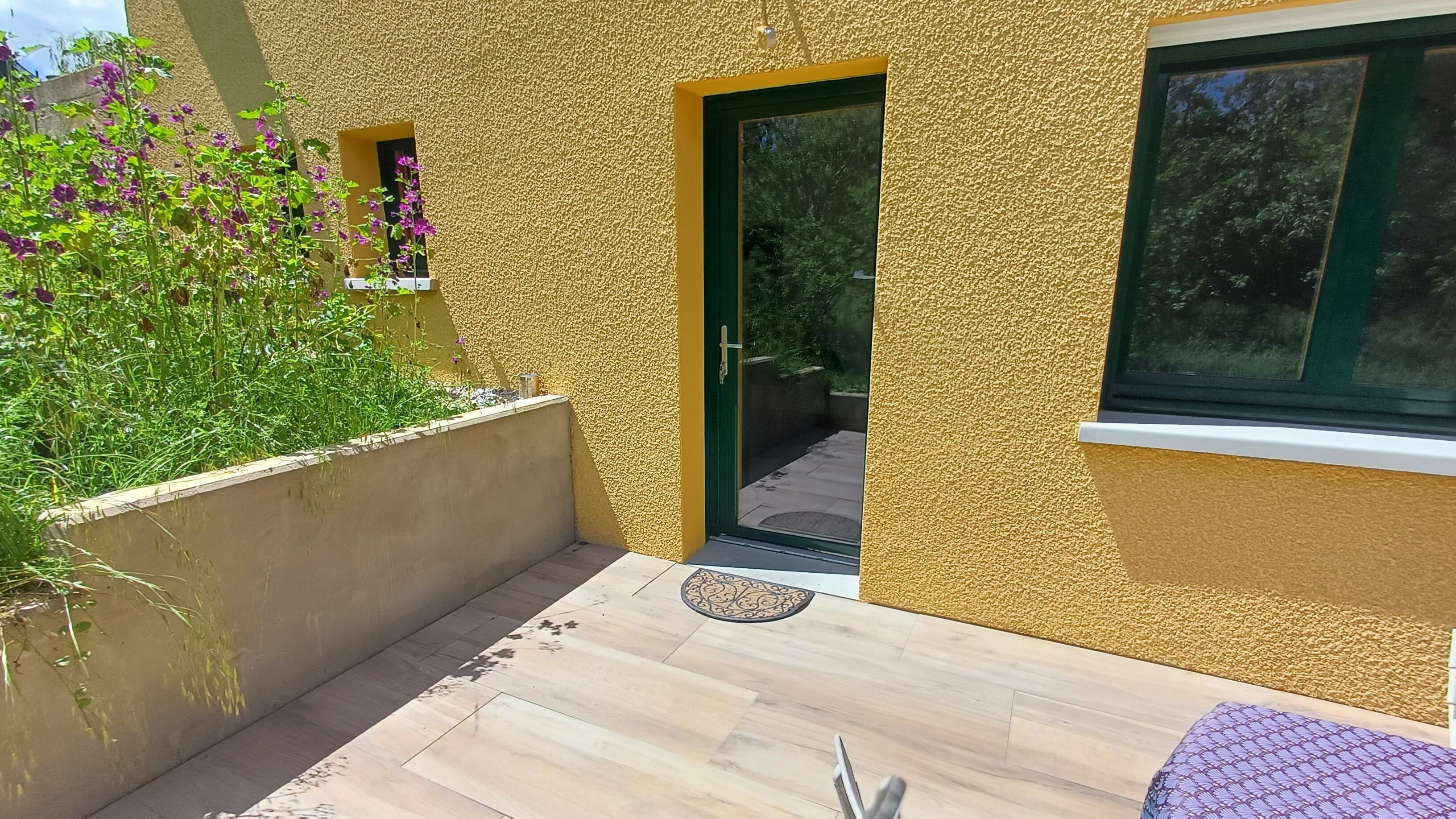 A modern building with a textured yellow exterior, a green door, and a window.