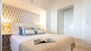 Un lit bien fait, avec une couvre-lit beige et des oreillers, une lampe de chevet et un papier peint à motifs.