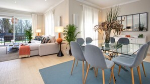 Un salon moderne avec un canapé, une table à manger en verre et des chaises. On y trouve une lampe, une plante en pot et une grande fenêtre avec des rideaux.
