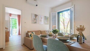 A modern living room with a sofa, dining table set for two, and a large window with curtains.