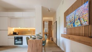 A modern kitchen with white cabinets, a wooden dining table set with plates and glasses, and a large cityscape painting on the wall.