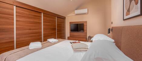 A modern hotel room with a large bed, wooden paneling, a flat-screen TV, and a mounted air conditioner.
